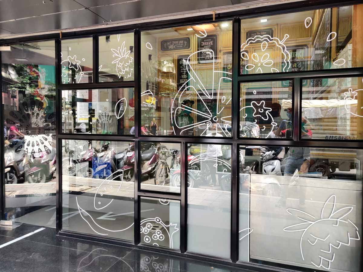 White ink printing of cliparts and doodles on transparent glass film pasted on the front partition of a naturals ice cream restaurant to give it a very beautiful look